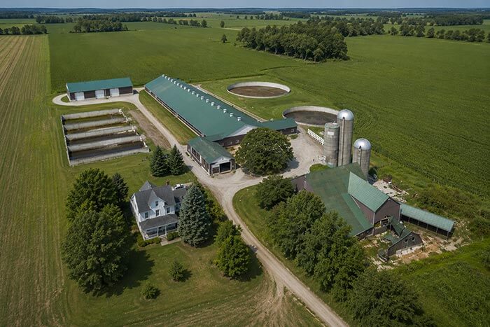 Aerial view of a dairy farm with a farm house, freestall barn, bank barn, stave tower silos, implement shed, manure storage.